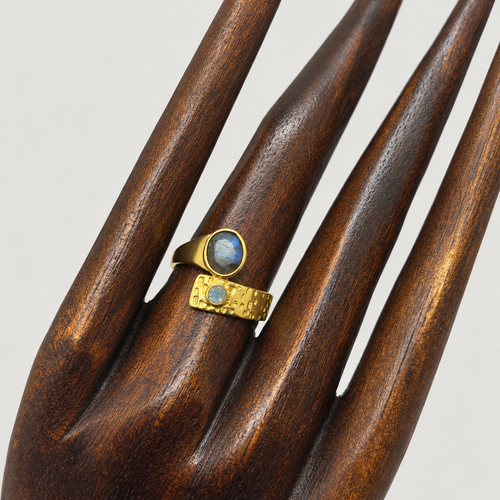 Anillo Eclipse con dos labradoritas naturales y bronce con baño de oro, colocado sobre una mano de madera.