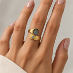 Anillo Eclipse de tono dorado con dos piedras gris azuladas, en una mano con manicura de color natural.