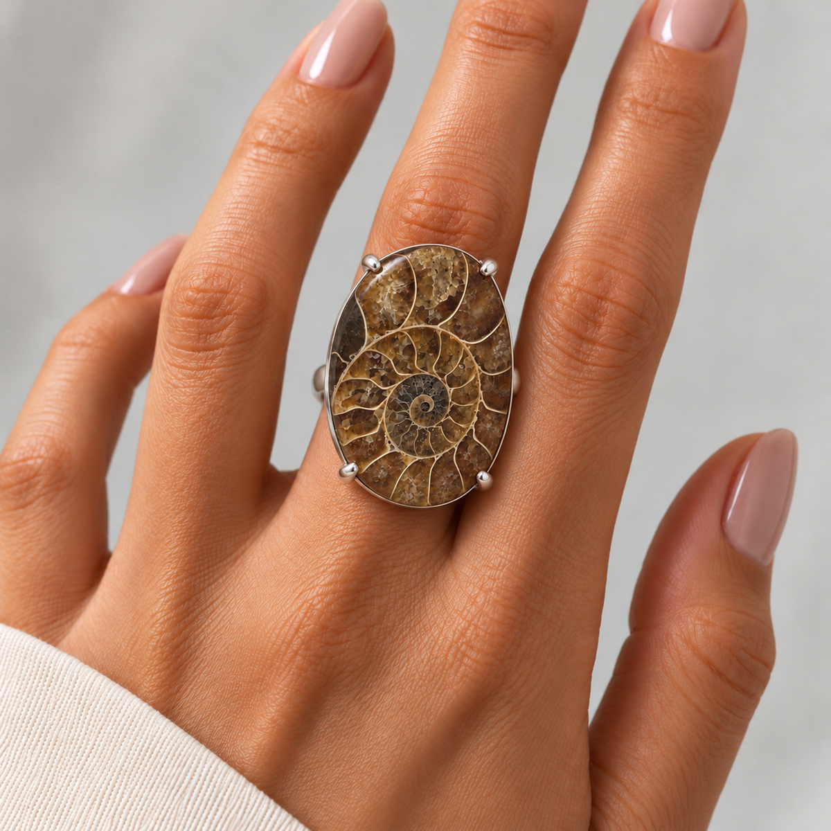 Anillo Madagascar de plata con amonita fósil de 3,5 por 2,5 cm centrado en un dedo, con manicura natural.