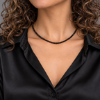 Choker de ónix negro facetado de 3 mm sobre modelo de cabello rizado y blusa de seda negra, encuadrada desde la barbilla.