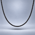 Detalle del choker de ónix negro facetado de 3 mm, suspendido sobre fondo gris suave con sombra y encuadre cercano.