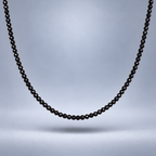 Detalle del choker de ónix negro facetado de 3 mm, suspendido sobre fondo gris suave con sombra y encuadre cercano.
