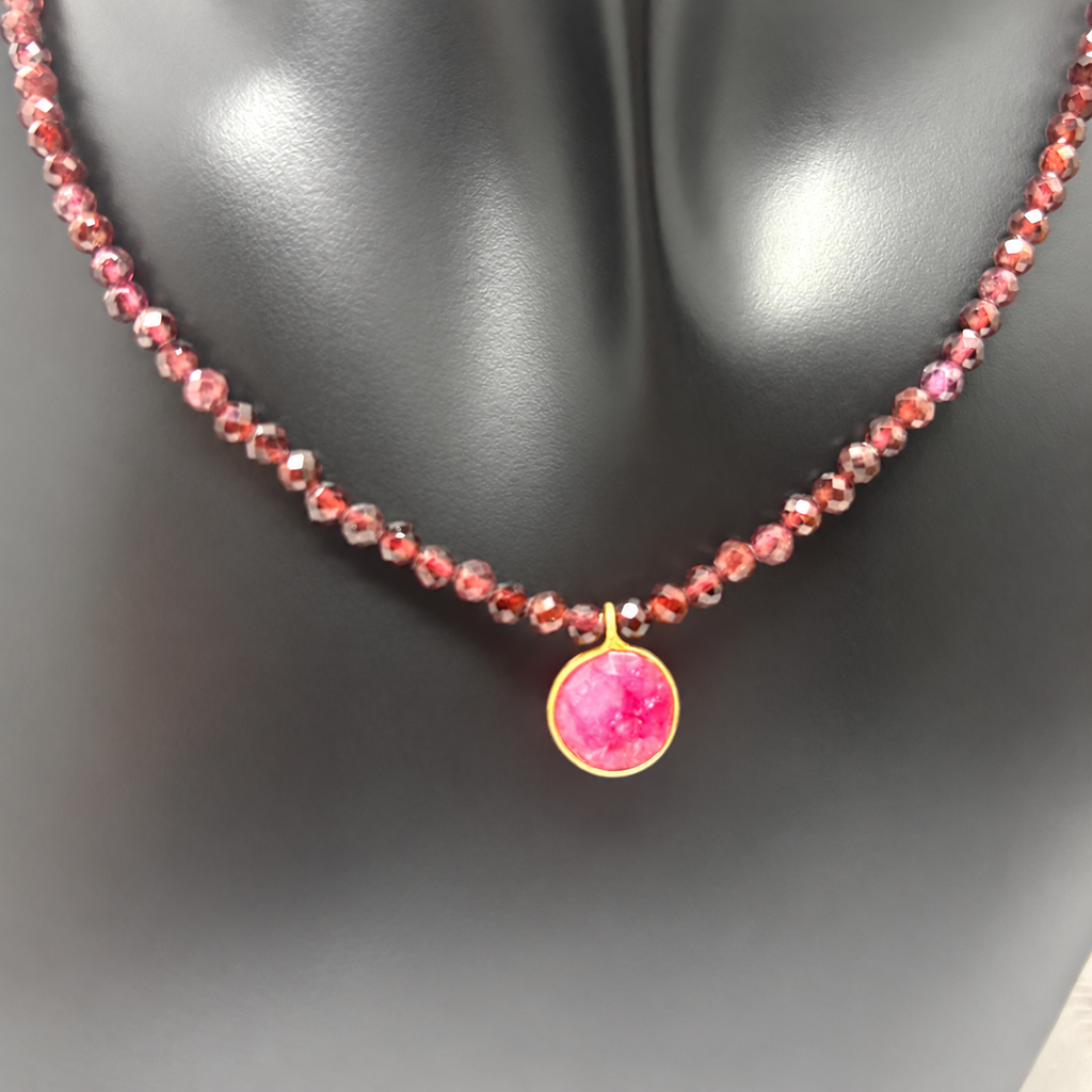 Fotografía del Collar Cap Roig sobre busto negro, con cuentas facetadas de granate y un colgante circular de rubí reconstituido en plata chapada en oro.