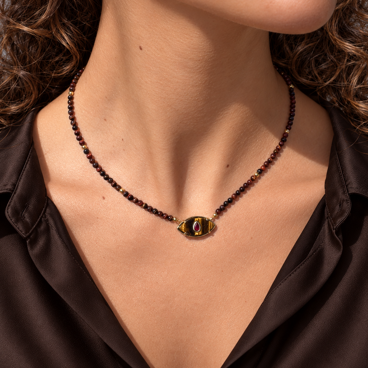Collar corto de ojo de tigre y rubí reconstituido sobre una modelo con blusa de seda marrón chocolate.