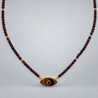 Collar de ojo de tigre y rubí reconstituido, suspendido sobre fondo gris claro.