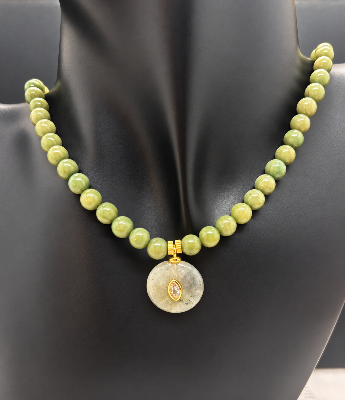 Fotografía real retocada suavemente del Collar Sa Riera sobre busto negro, con cuentas de jade, colgante circular con cristal central y dos piezas redondas doradas.