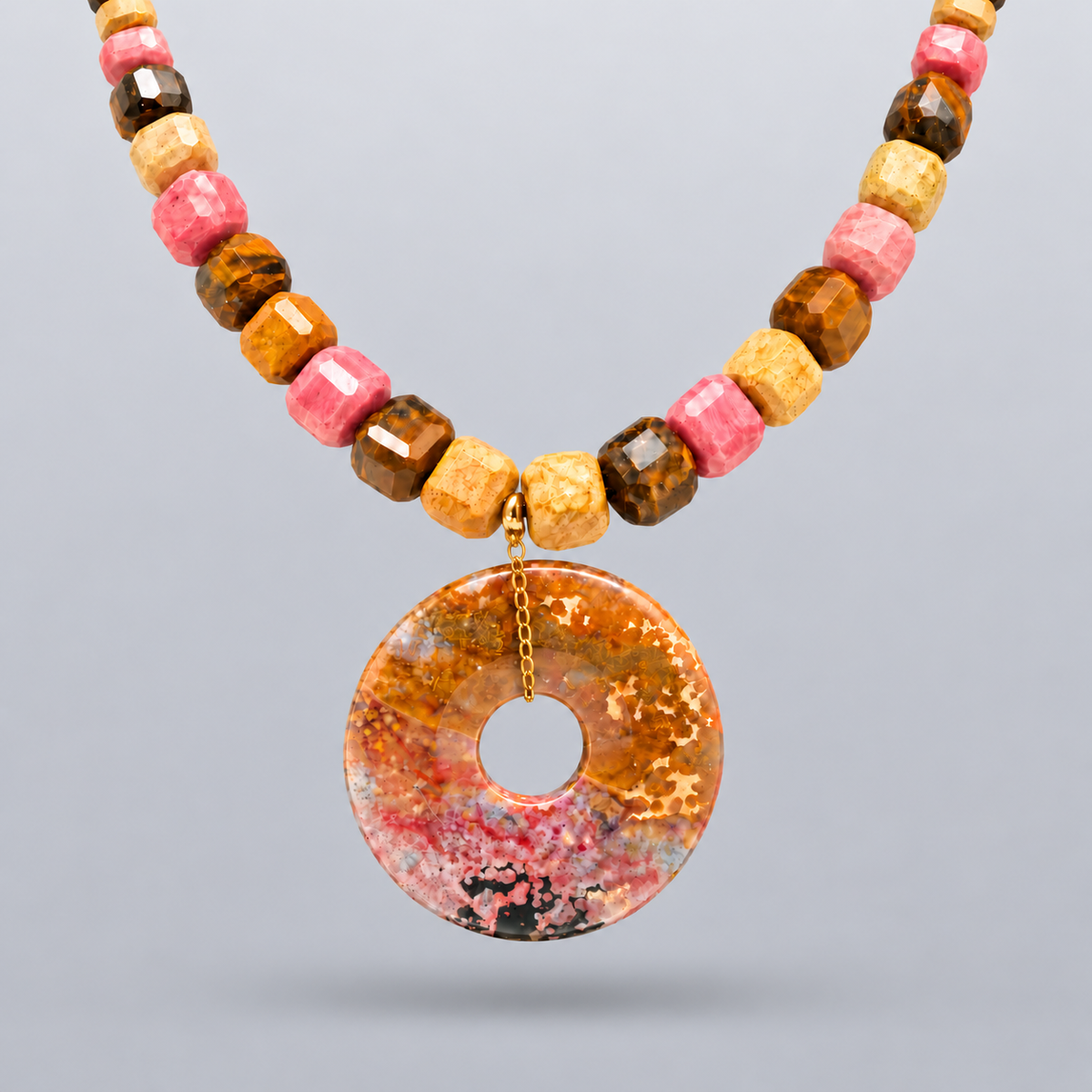 Collar Tamariu de rodocrosita rosa, ojo de tigre marrón y jaspe beige, con colgante circular de ágata india, suspendido sobre fondo gris claro degradado.