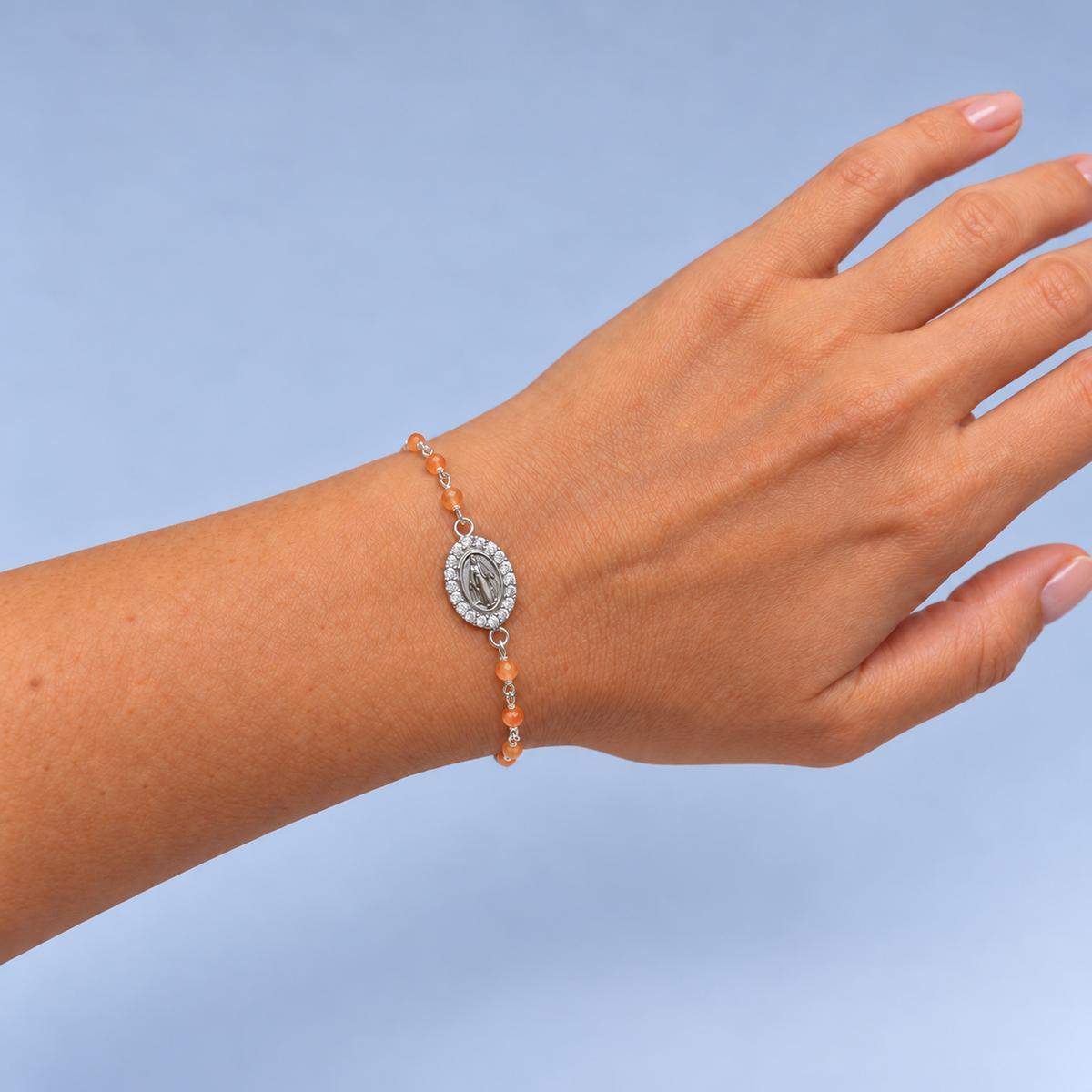 Pulsera Alma de plata y cornalina naranja pastel con medalla de la Virgen, puesta en la muñeca de la modelo