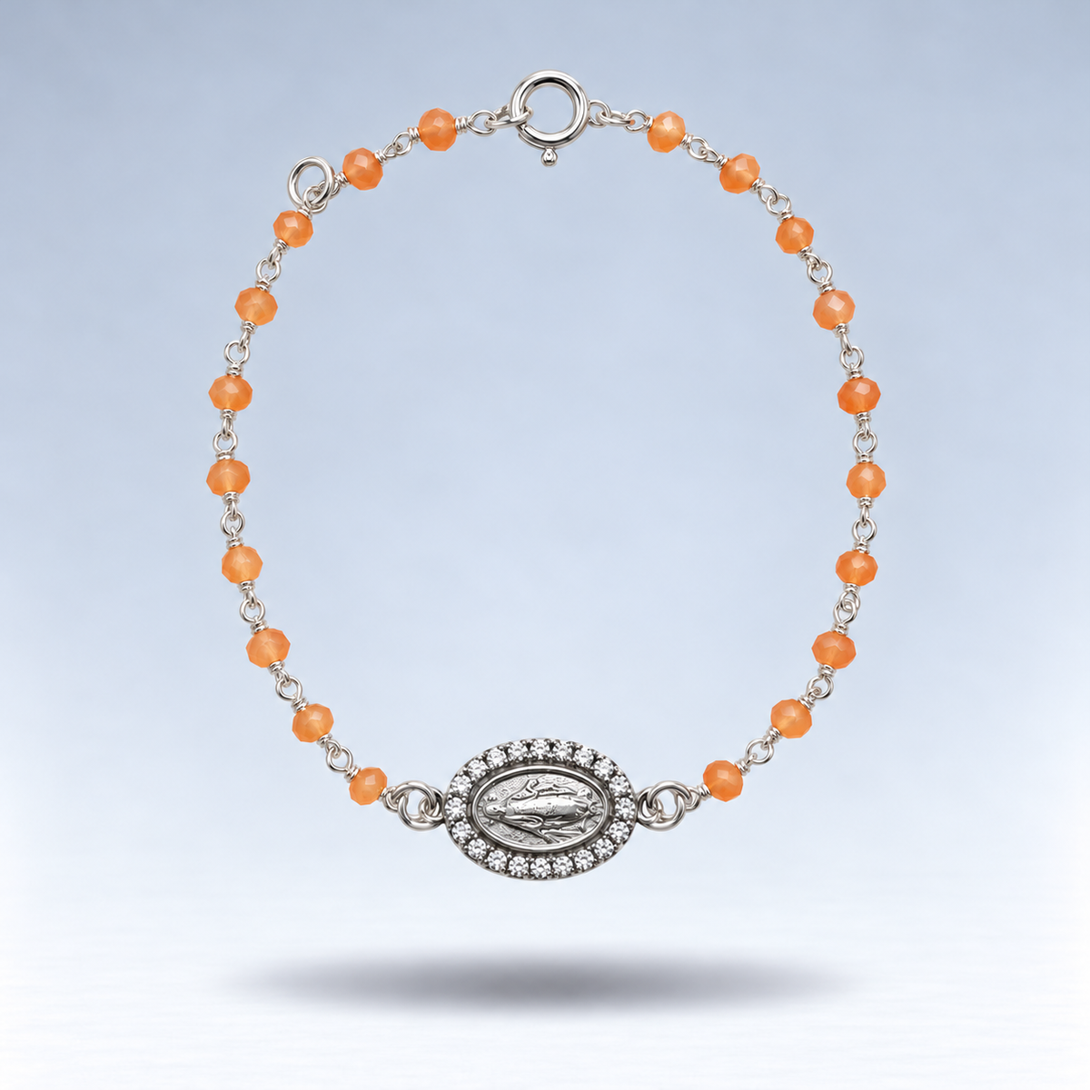 Pulsera Alma de plata con cornalina naranja pastel y medalla de la Virgen con circonitas, suspendida sobre fondo gris claro